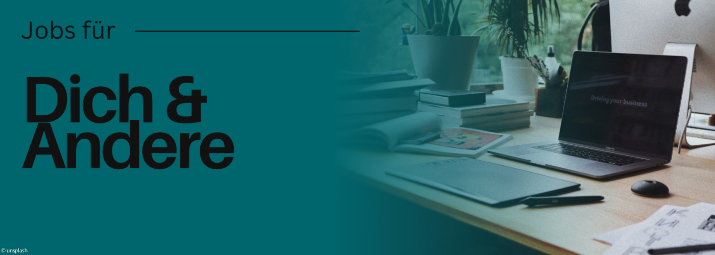 Schreibtisch mit Laptop und Handy darauf. Es liegen außerdem Bücher darauf und Zeitschriften.