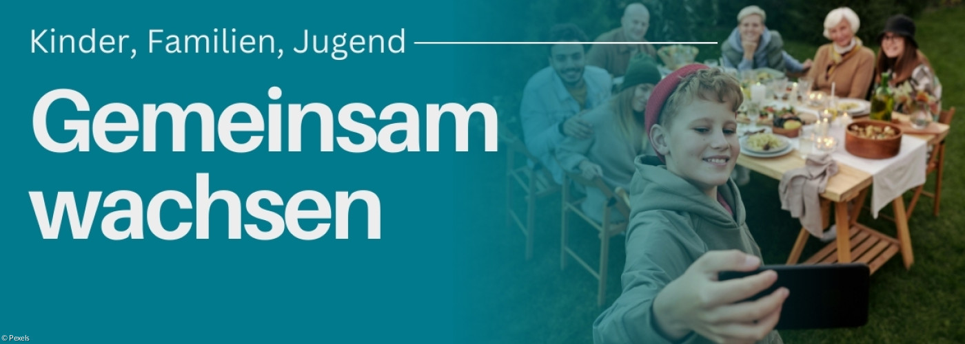 Jugendlicher der ein Selfie macht, mit einem Tisch von Menschen im Hintergrund auf einem grünen Rasen.