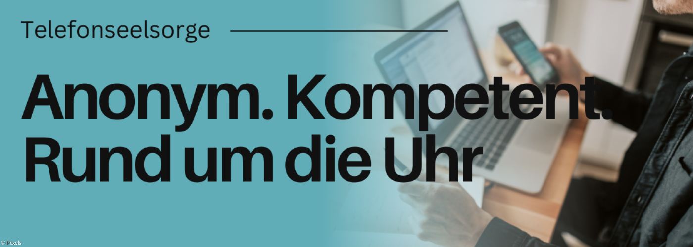 Jemand sitzt an einem Schreibtisch mit Handy und Laptop vor sich.