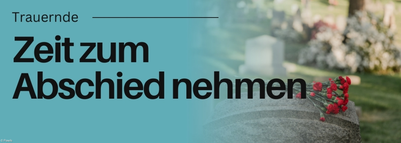 Grabstein mit Blumen darauf. Friedhof im Hintergrund.