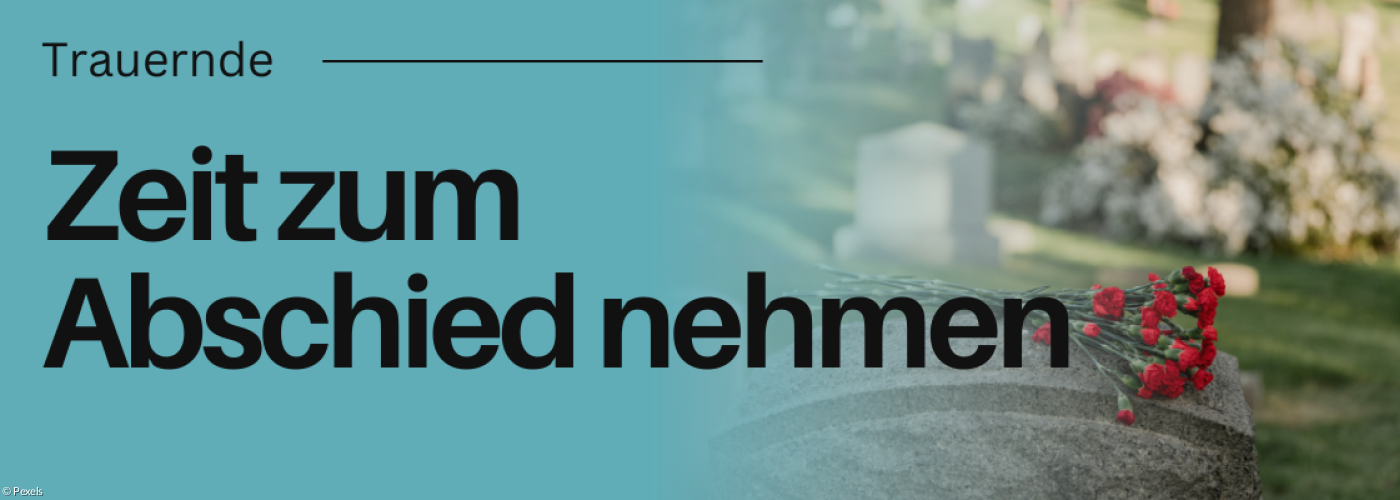 Grabstein mit Blumen darauf. Friedhof im Hintergrund.