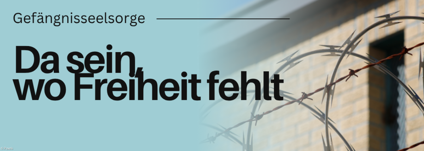 Stacheldrahtzaun im Vordergrund. Dahinter sieht man ein Gebäude.