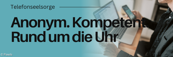 Jemand sitzt an einem Schreibtisch mit Handy und Laptop vor sich.