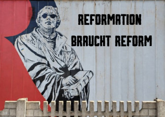 Ein Graffiti an einer Wand mit Luther in schwarz-weiß, der eine Sonnenbrille trägt. Daneben steht auf der Wand: Reformation braucht Reform in fetten schwarzen Lettern.