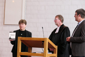 Es stehen drei Personen hinter einem Stehpult. Links eine Frau, die ein Buch hält, rechts von ihr ein Pfarrer Klaus Göldner und Jörg Mahler vom Martin Luther Verein als Dolmetscher