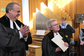 v.l. Dekan Jörg Breu klatscht und Pfarrerin Dr. Bärbel Mayer-Schärtel strahlt mit der Urkunde in der Hand.